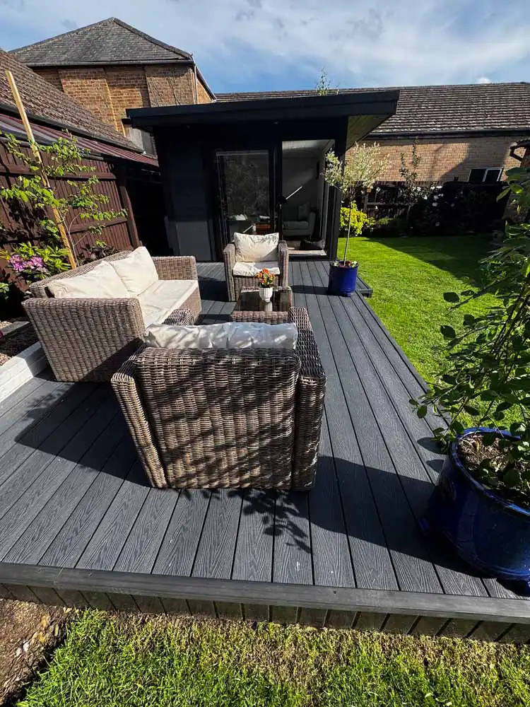 Dark grey composite decking with rattan garden furniture beside a dark grey garden room