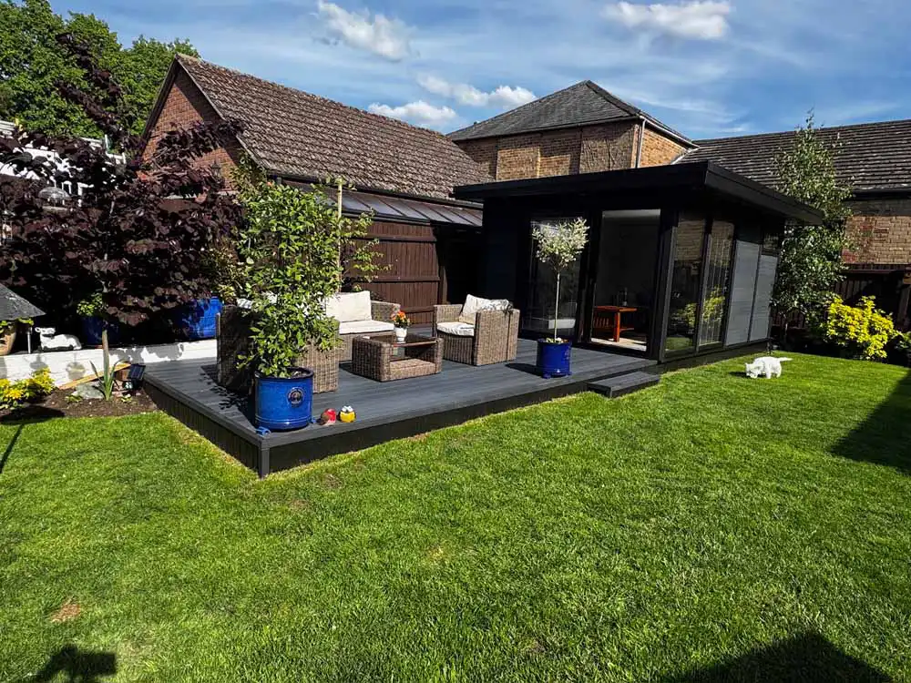 Dark grey composite garden room with a large composite deck, garden furniture and potted plants on a lawn